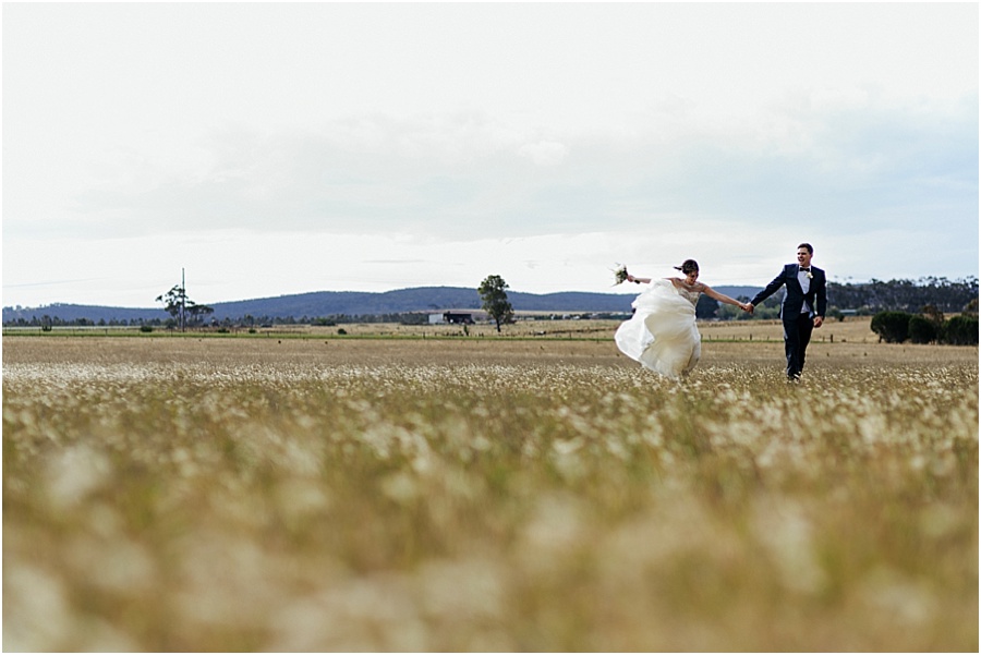 Shooting thru grass, wind swirling brides dress at Farm wedding 