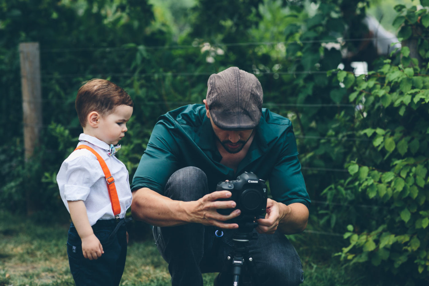 A videographer sets up his camera whilst an adorable toddlers watches on