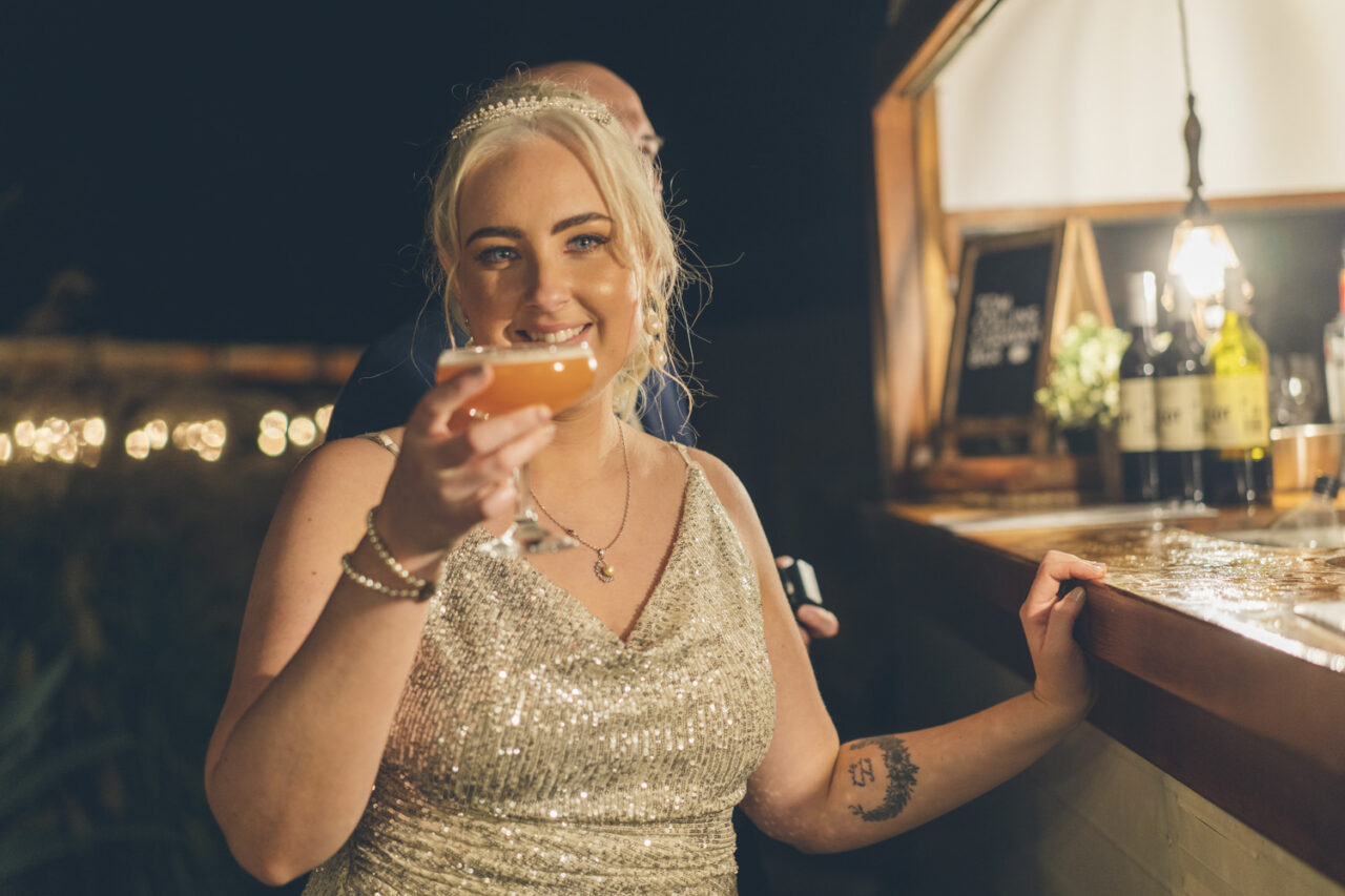Bride holding cocktail and smiling during wedding reception at night