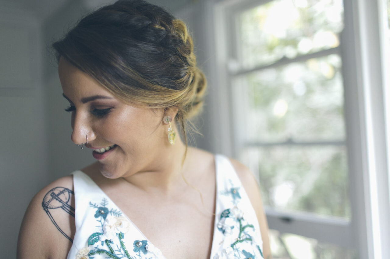 Bride portrait by window light showing dress details and tattoos before ceremony