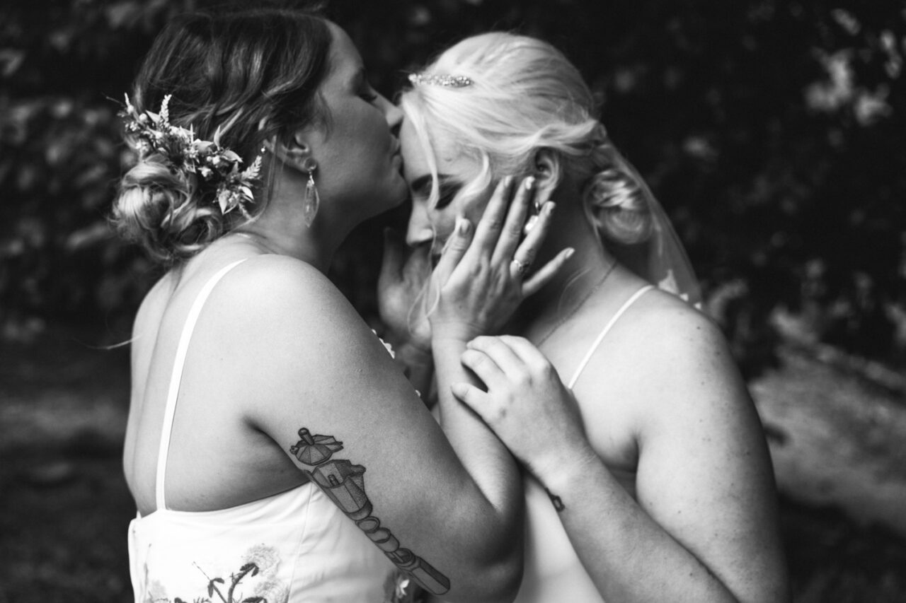 One bride kissing the other on the forehead during intimate wedding portrait