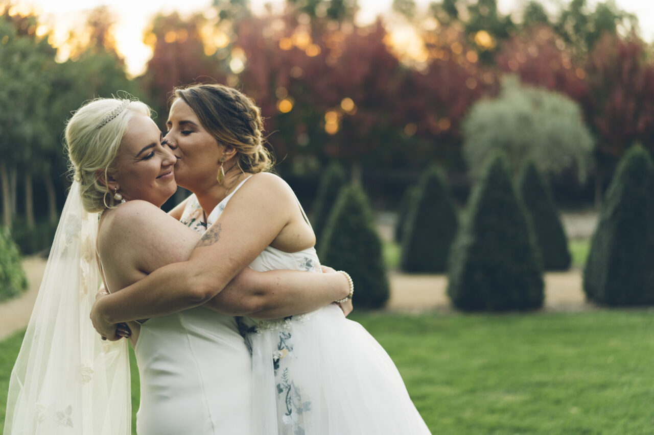 One bride kissing the other during golden hour garden portrait at wedding