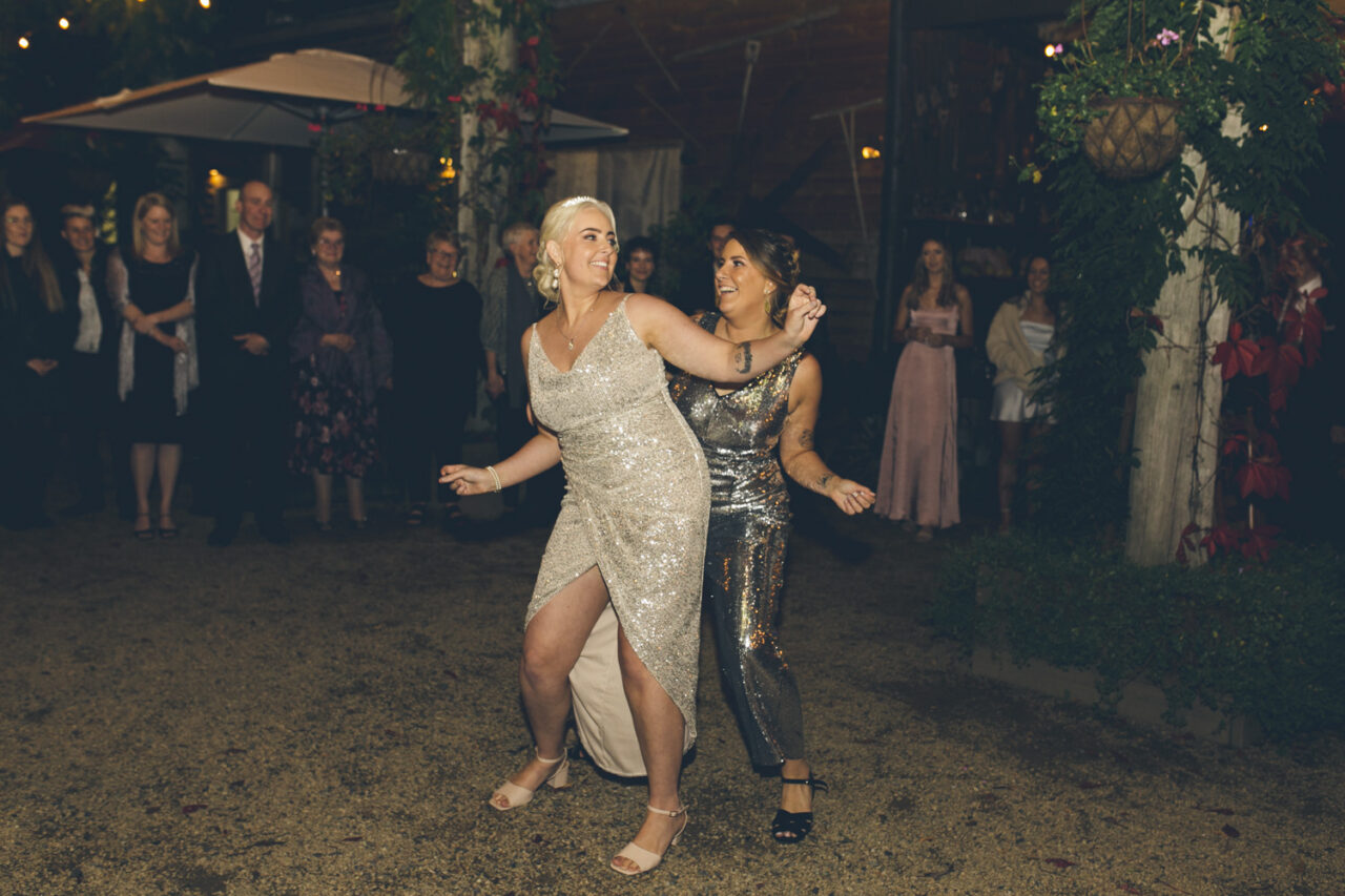 Brides dancing together at night surrounded by guests during wedding reception