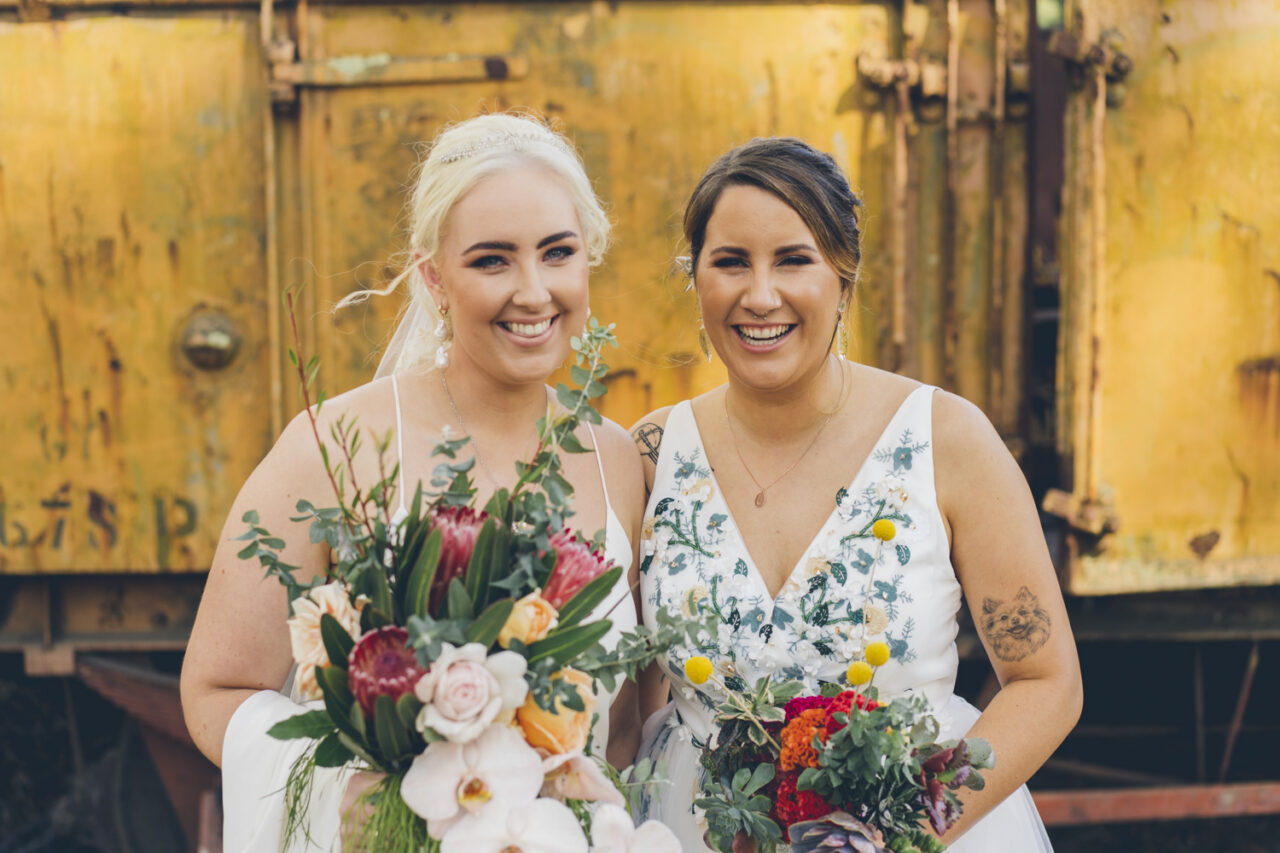 Brides smiling together holding colourful bouquets during wedding portraits