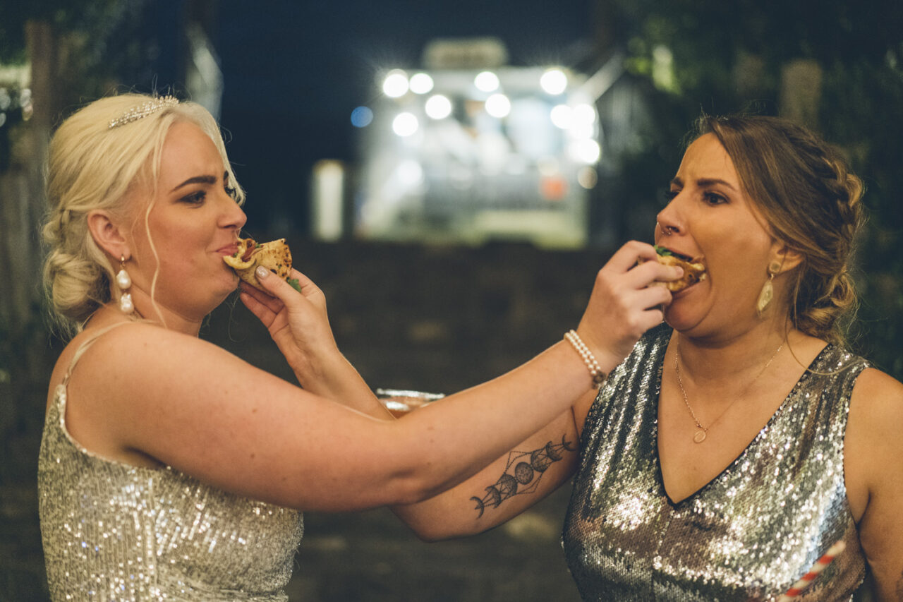Brides feeding each other pizza during fun wedding reception moment