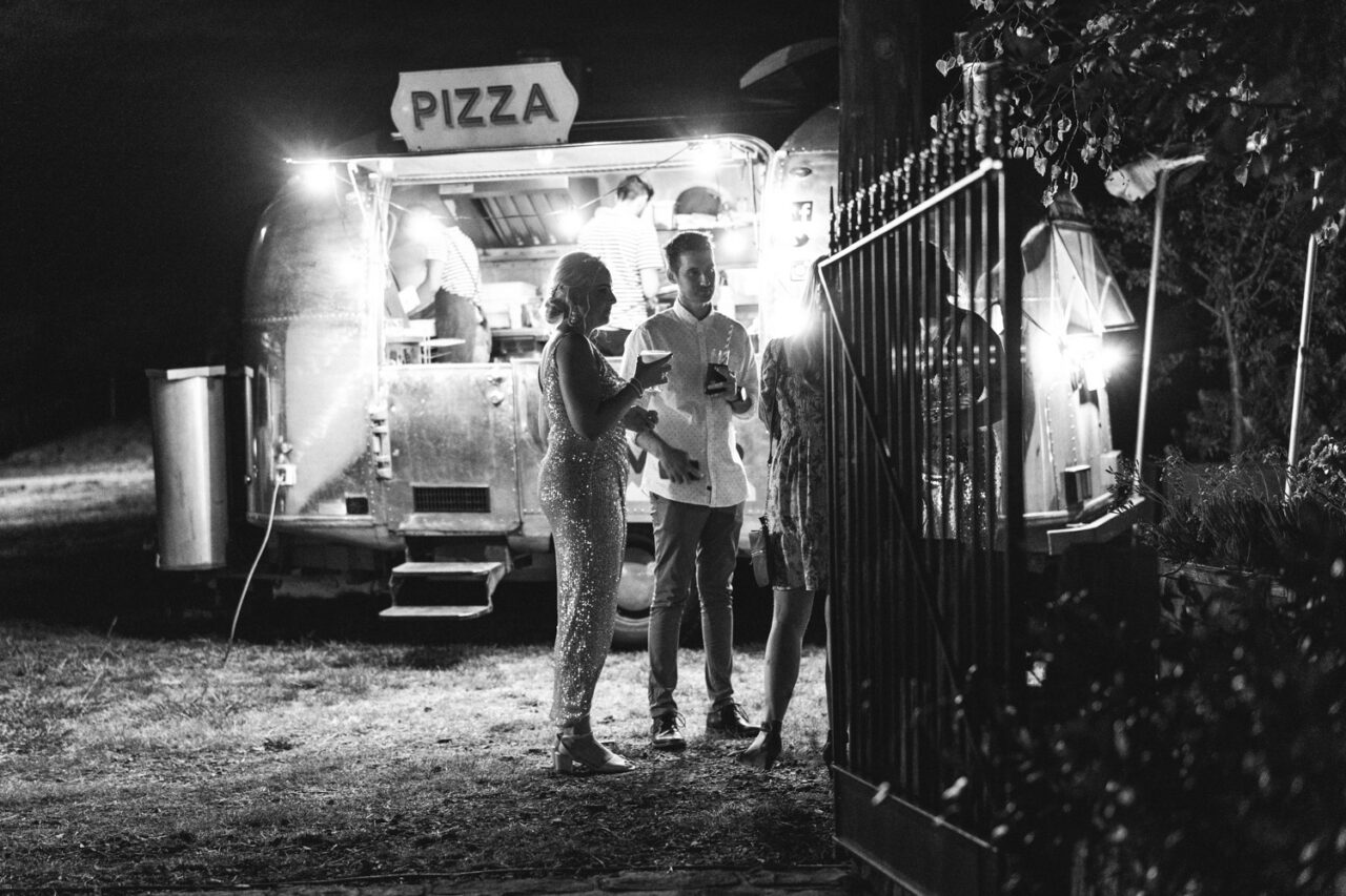 Wedding guests gathered around pizza van at night during reception