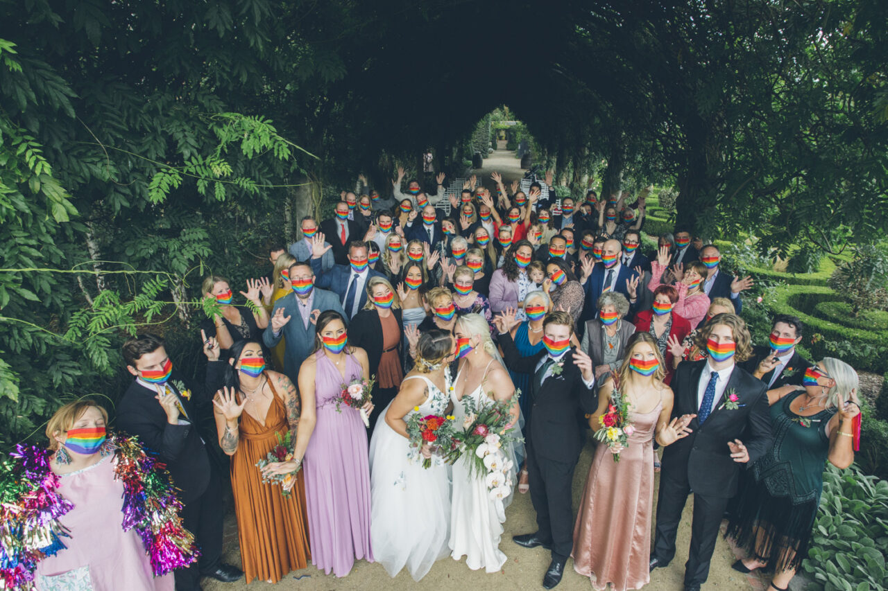 Wedding guests wearing rainbow masks gathered for group photo at Alowyn Gardens