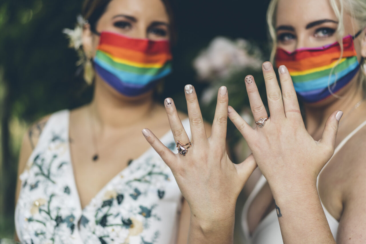 Brides showing wedding rings while wearing rainbow face masks