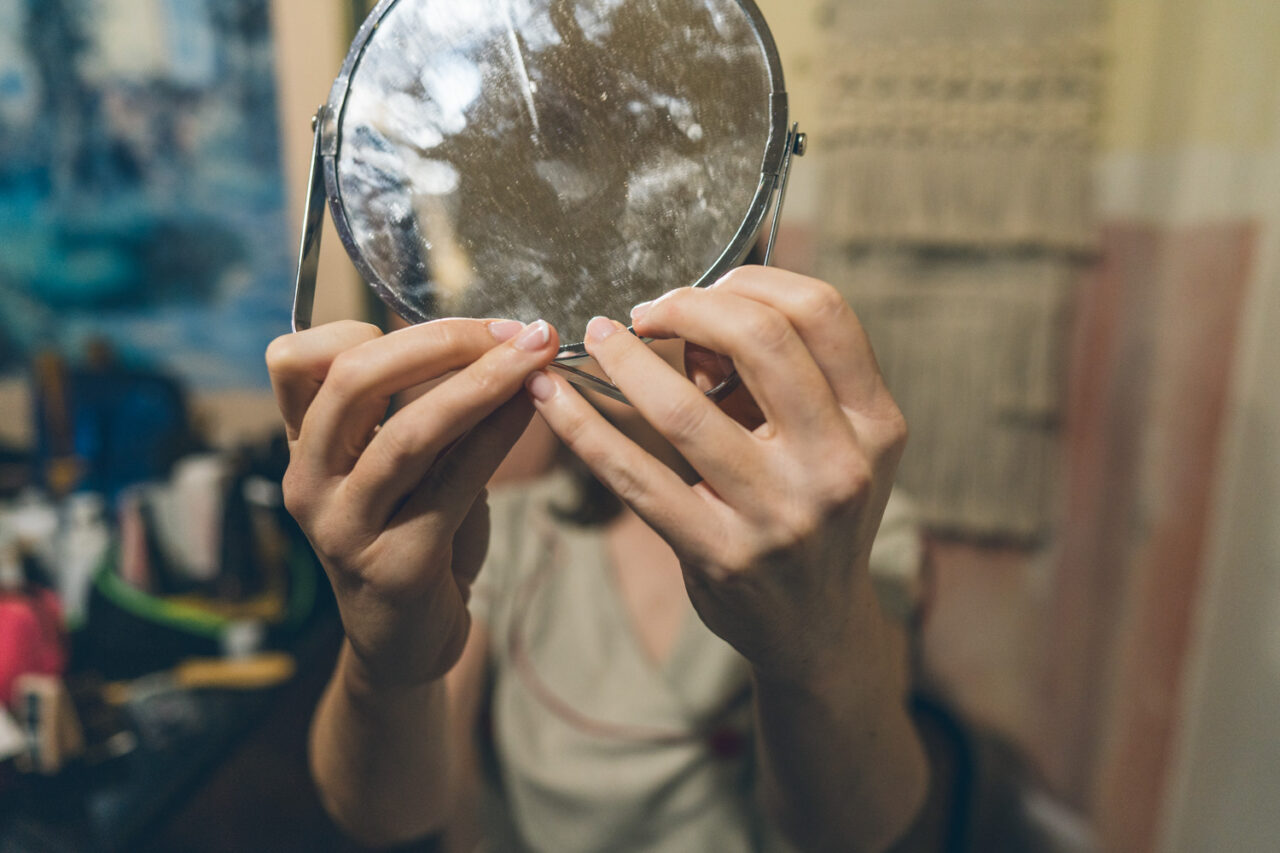 Candid close-up of the bride holding a handheld mirror while getting ready for Bel and Leigh’s wedding