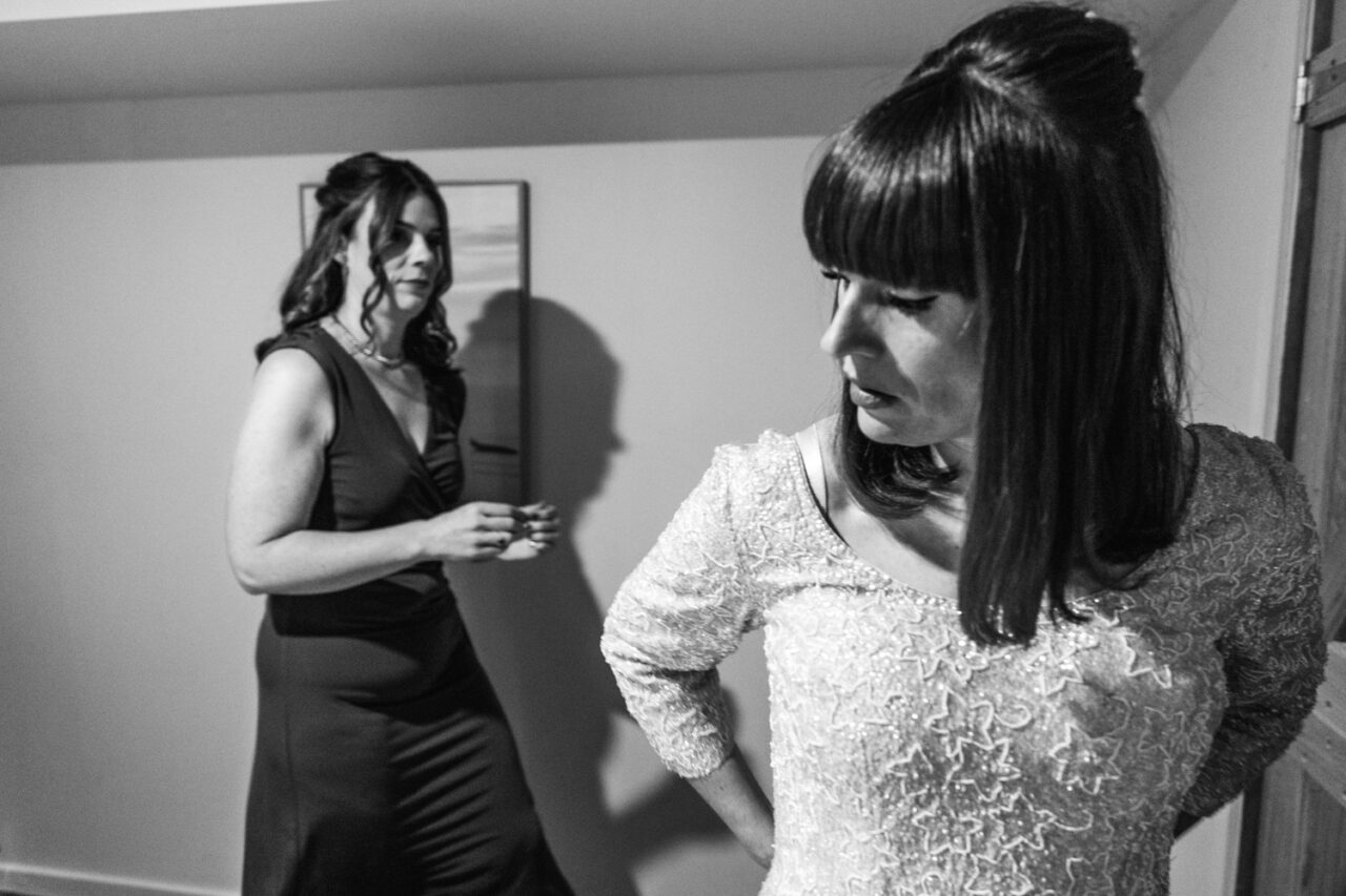 Black and white moment of the bride and her friend helping each other get ready before Bel and Leigh’s wedding.