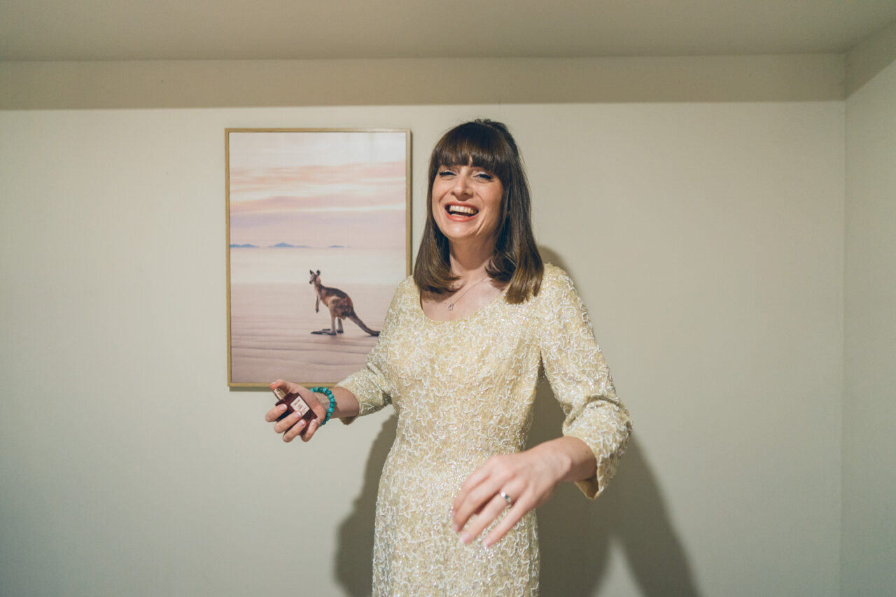 Bride laughing and holding perfume while getting ready for Bel and Leigh’s wedding day.