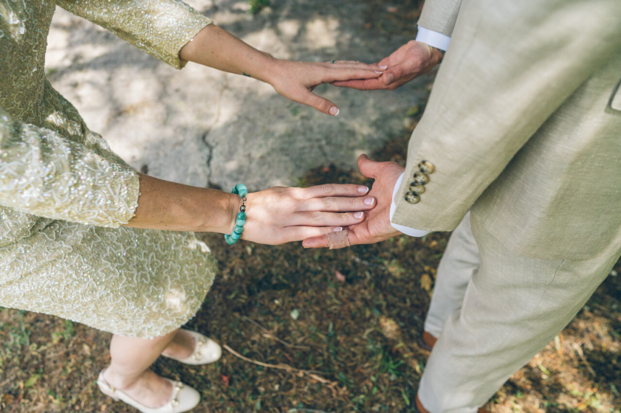Close-up of couple reaching out to hold hands during their first look, showing wedding outfits and connection.