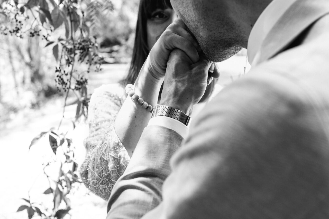 Groom kissing bride’s hand in an intimate black and white wedding portrait.