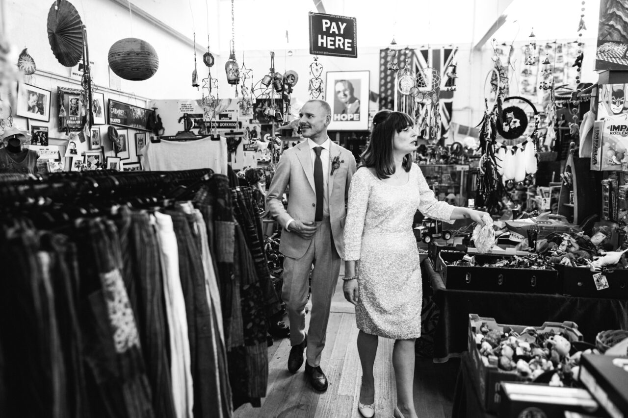 Black and white photo of wedding couple browsing inside quirky vintage store filled with collectibles