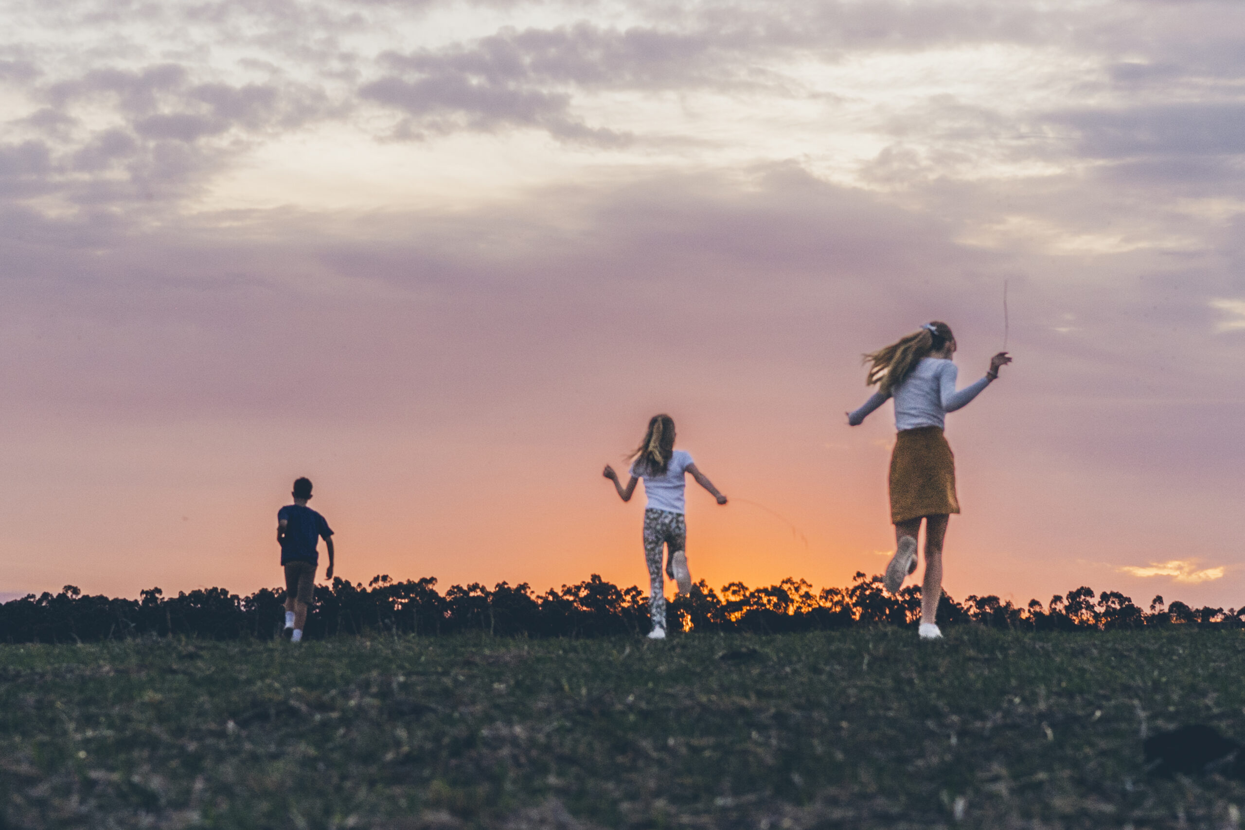 Three kids running through a grassy field at sunset during a candid family portrait session on the Surf Coast.