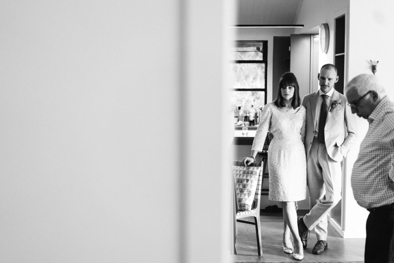 Bride and groom standing quietly in a kitchen before the ceremony, captured in black and white documentary style.