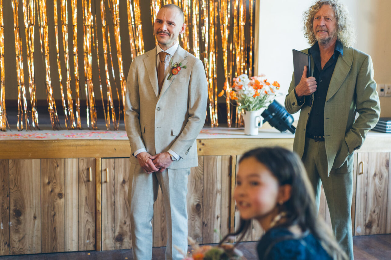Groom smiling with emotion as he watches his partner walk down the aisle beside the celebrant