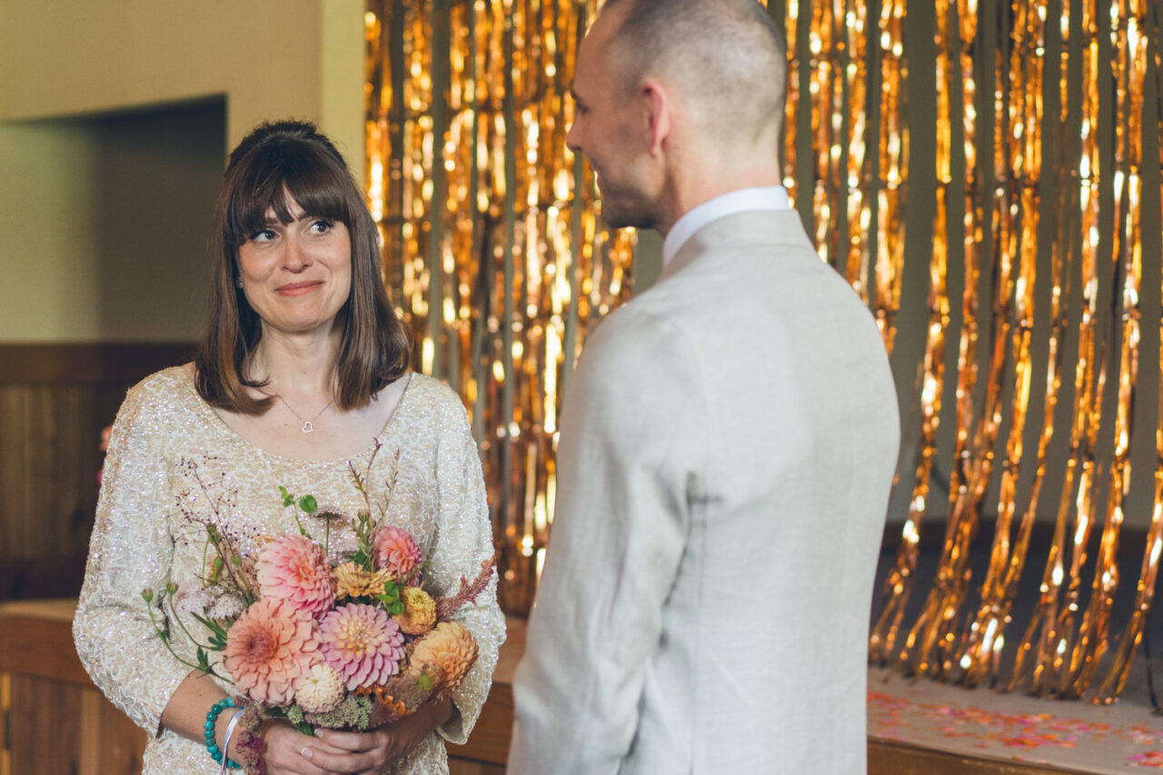Bride smiling softly during the wedding vows, holding a colourful bouquet of dahlias.