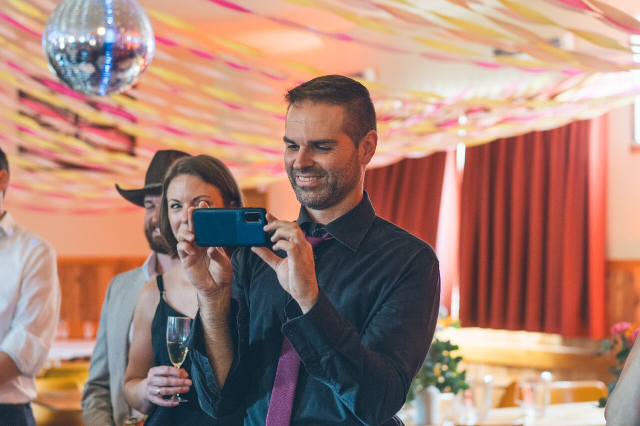 Guest capturing the ceremony on their phone under colourful streamers and disco lights.