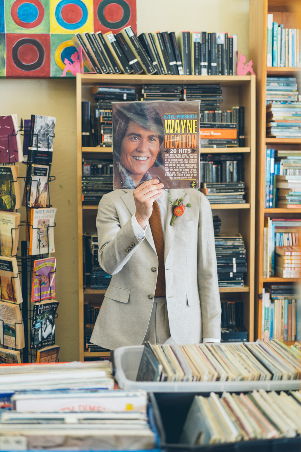 Groom playfully holds up a Wayne Newton record cover to his face, blending humour and nostalgia in a vintage store setting.