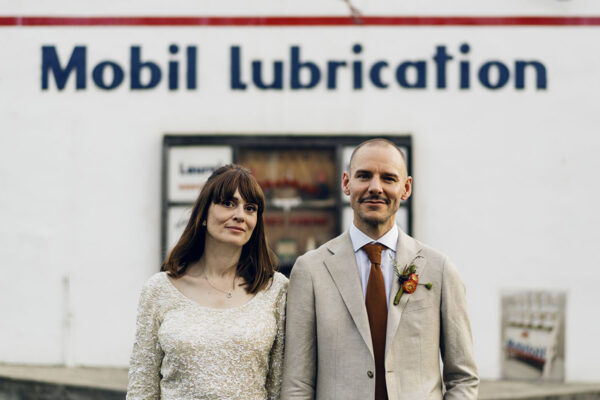 Bride and groom, Bel and Leigh, standing in front of an old Mobil Lubrication building during their candid wedding portrait session.
