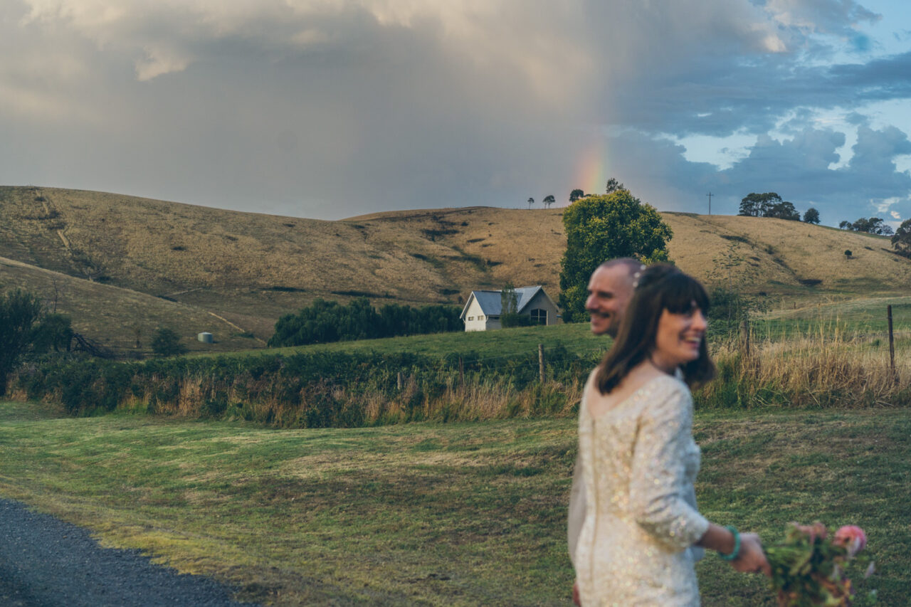 Wedding couple walking in countryside with rainbow appearing in the background
