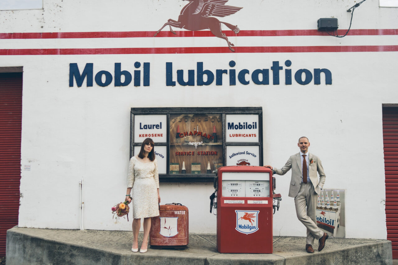 Bride and groom posing outside a vintage Mobil service station with old pumps