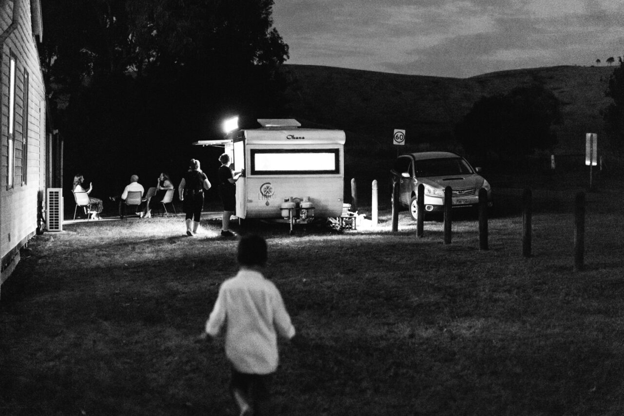 Guests gather near a lit vintage caravan at night outside the hall