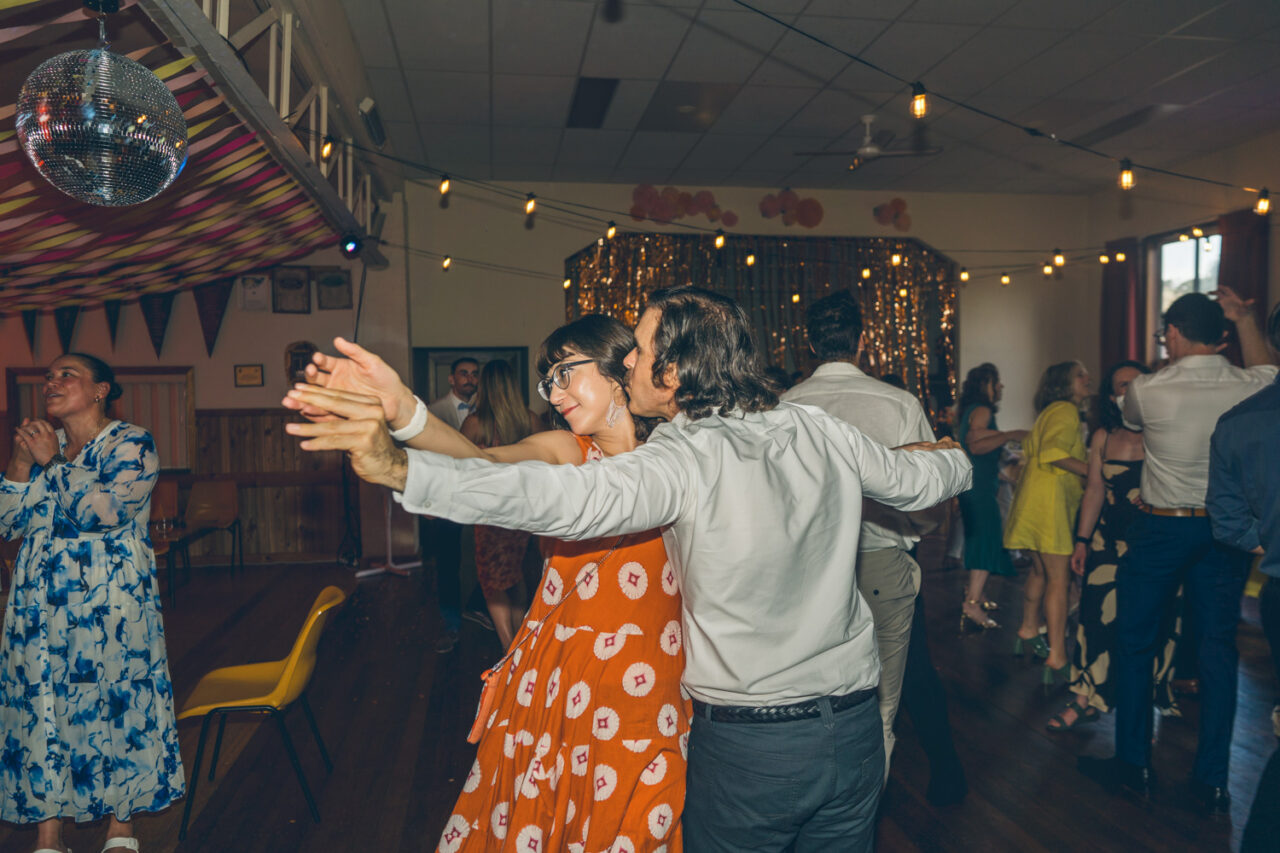 Wedding guests dancing under fairy lights at a community hall