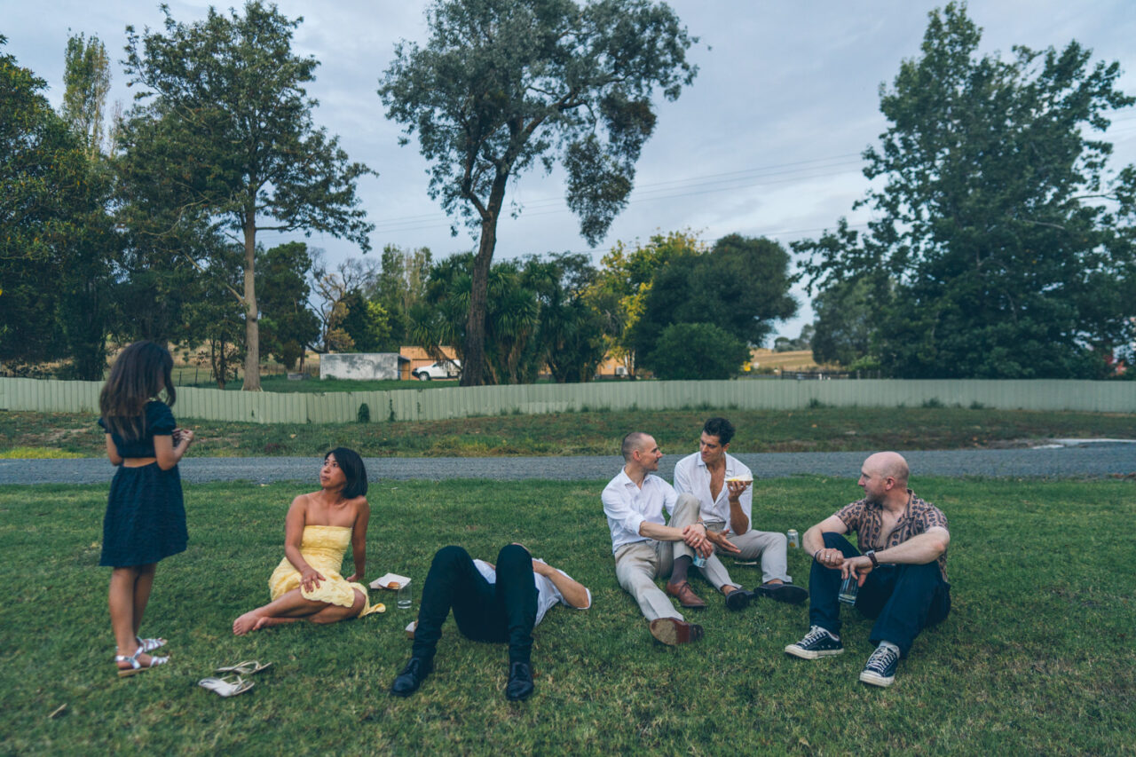 Wedding guests sitting on grass talking in the evening light