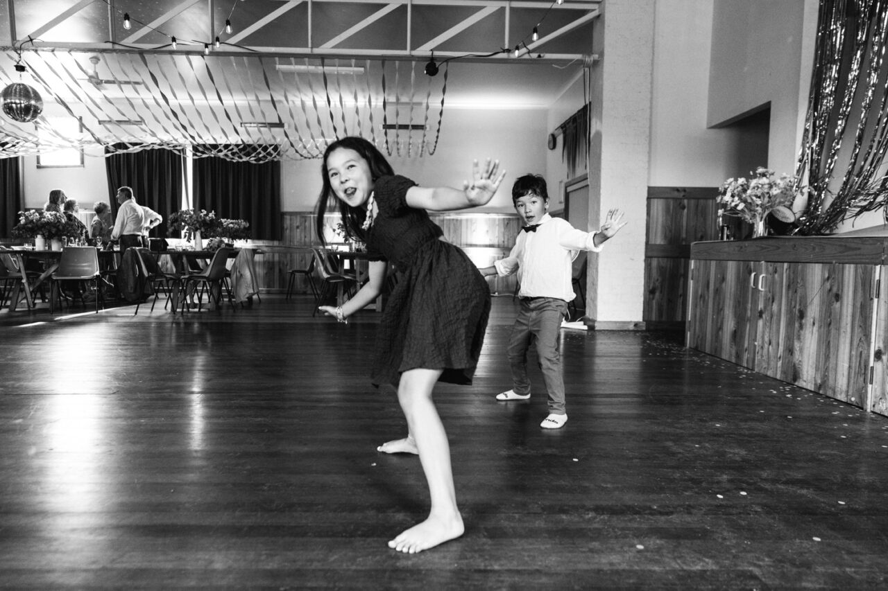 Two children dancing barefoot on the wooden floor during a wedding reception.
