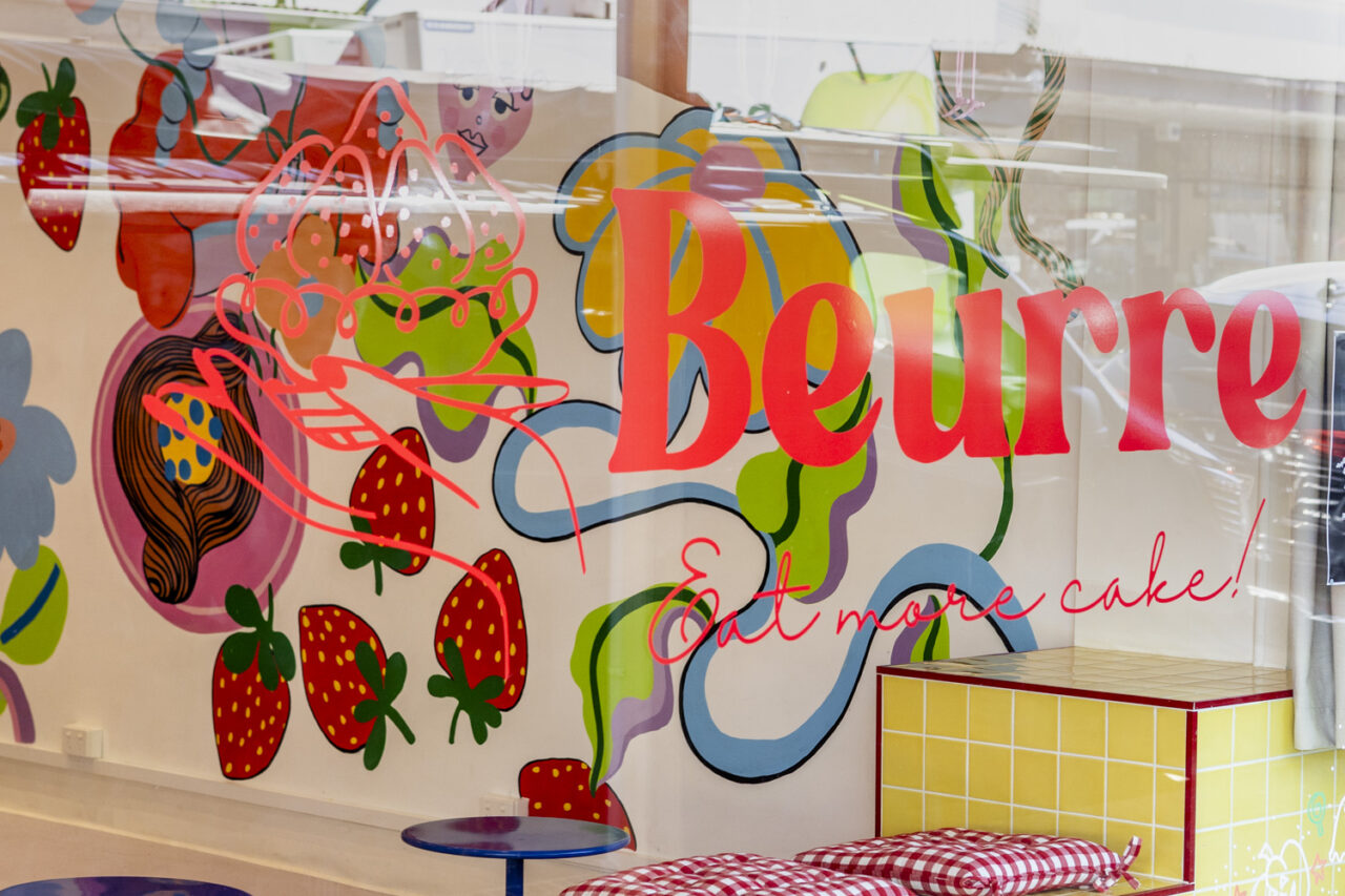 Close up of the Beurre Cakes window signage against the hand painted mural featuring bright strawberries and colour, photographed for documentary brand storytelling