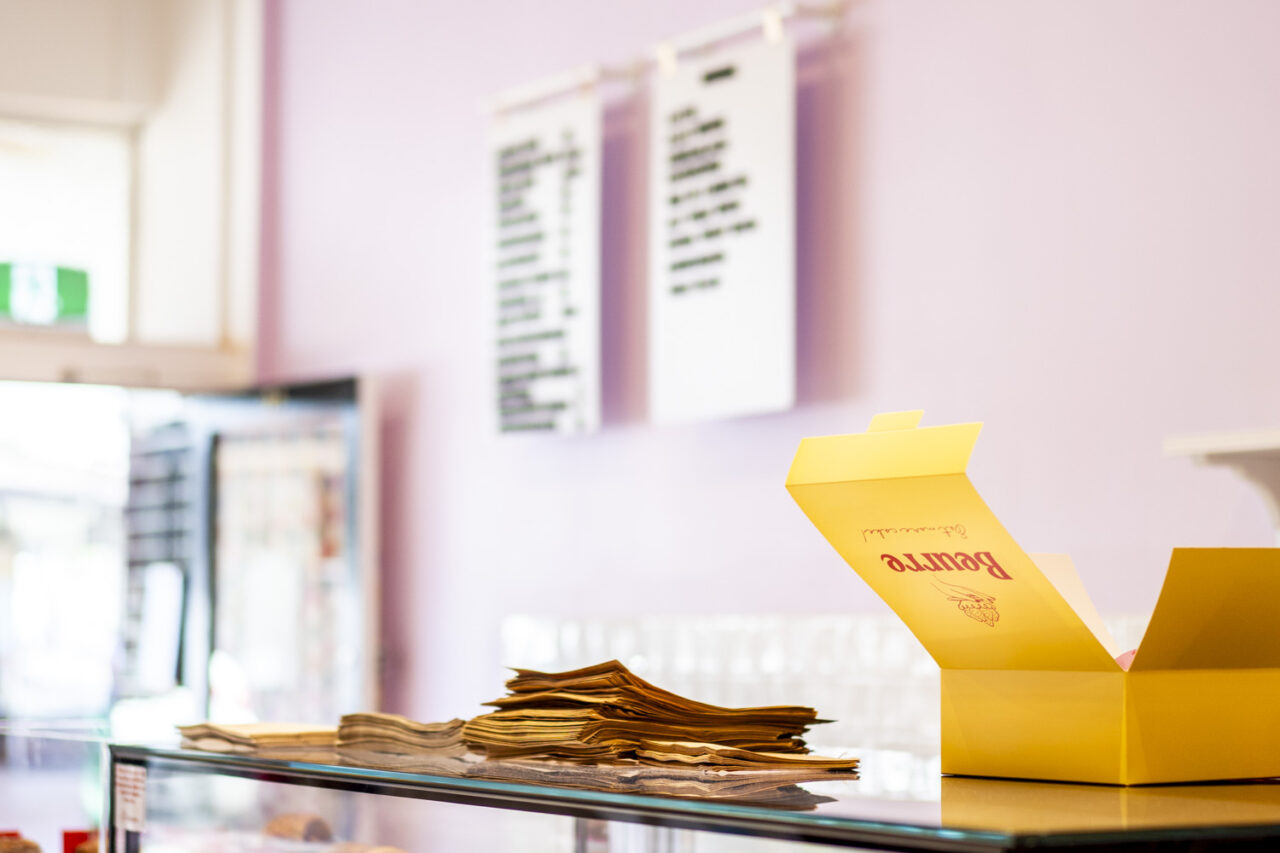Yellow Beurre Cakes pastry box sitting on the counter with the menu blurred in the background, photographed as documentary brand photography for a creative small business