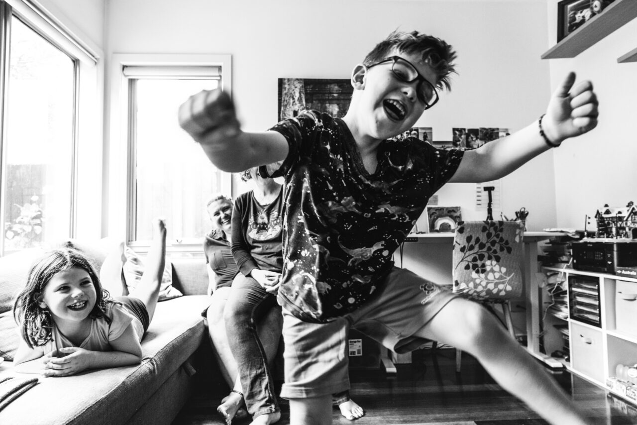 Children laughing and dancing at home while their family watches during a candid summer family photo session on the Surf Coast