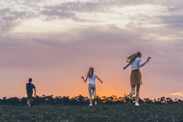 Kids running across an open field at sunset during a candid summer family photo session on the Surf Coast