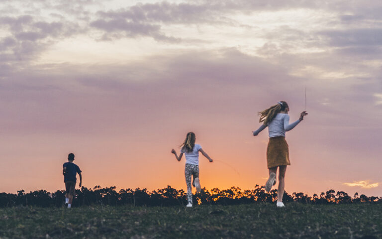 Kids running across an open field at sunset during a candid summer family photo session on the Surf Coast