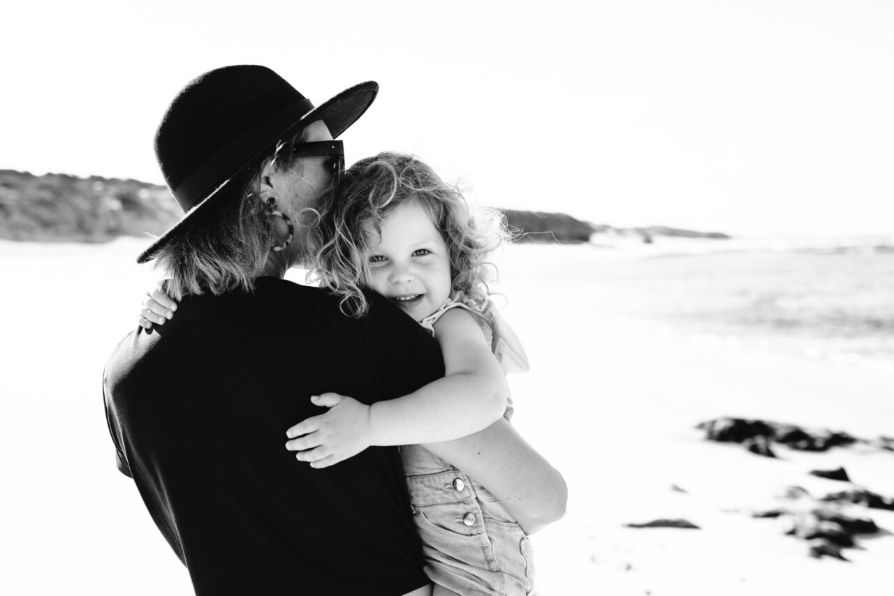 Mother holding her young daughter at the beach during a candid summer photo session on the Surf Coast