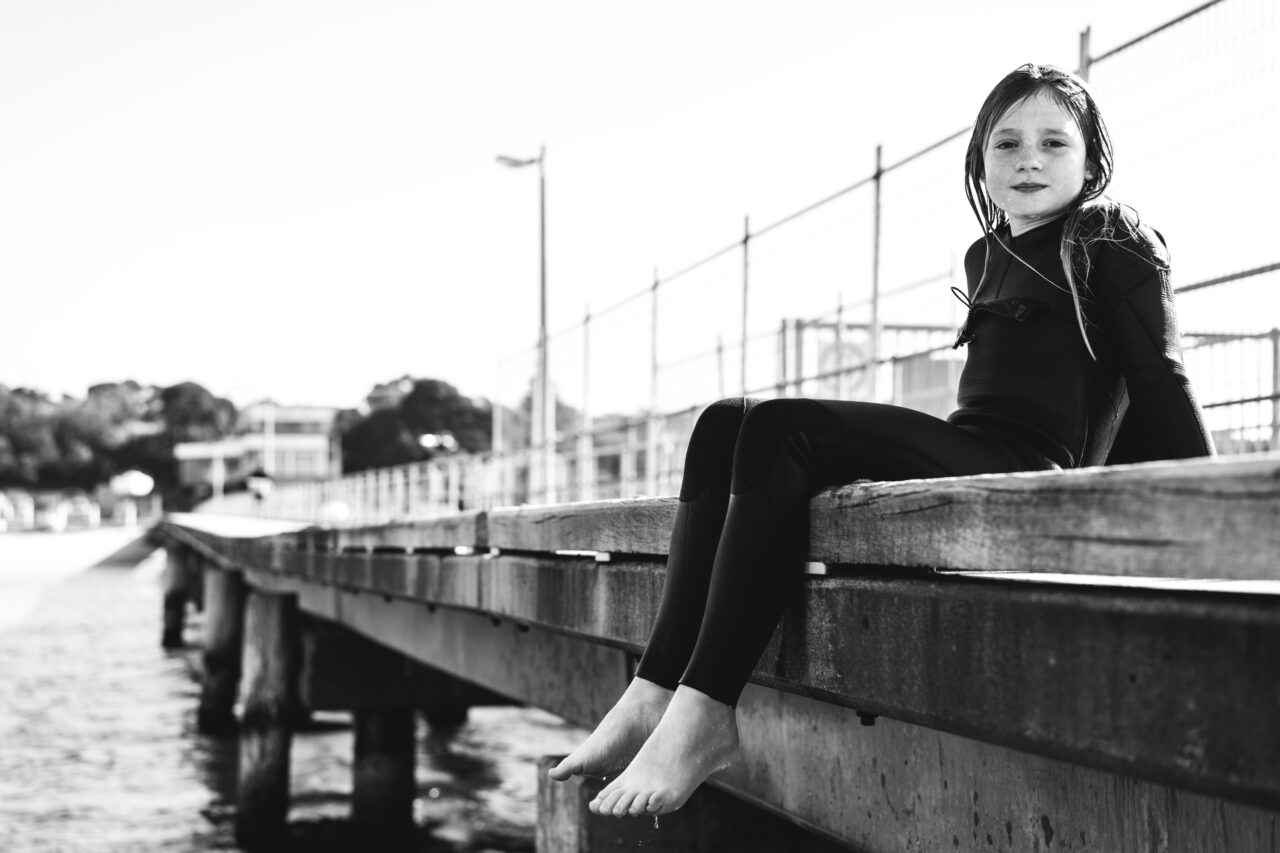 Child in wetsuit sitting on the jetty after swimming during a candid summer photo session Surf Coast