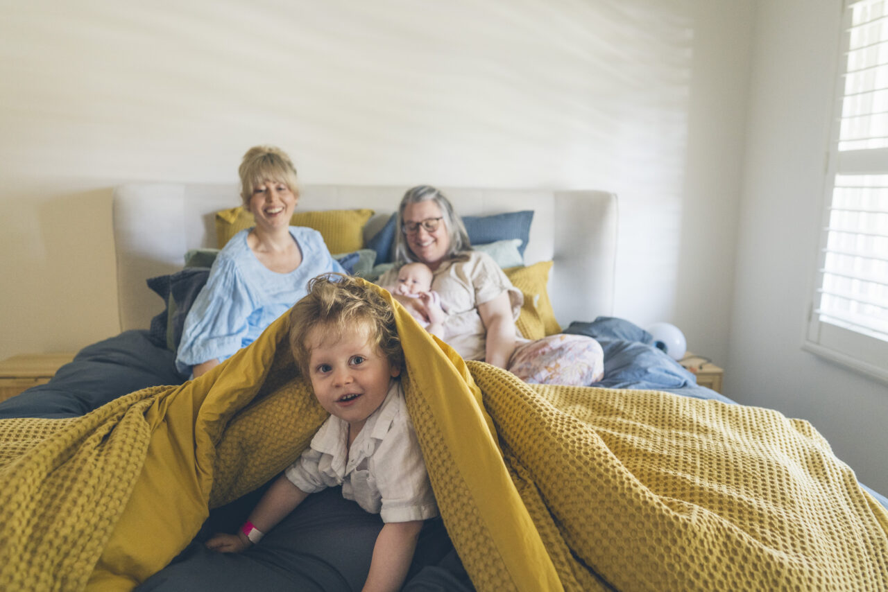 Family relaxing together in bed on a sunny morning during a candid summer storytelling photo session on the Surf Coast