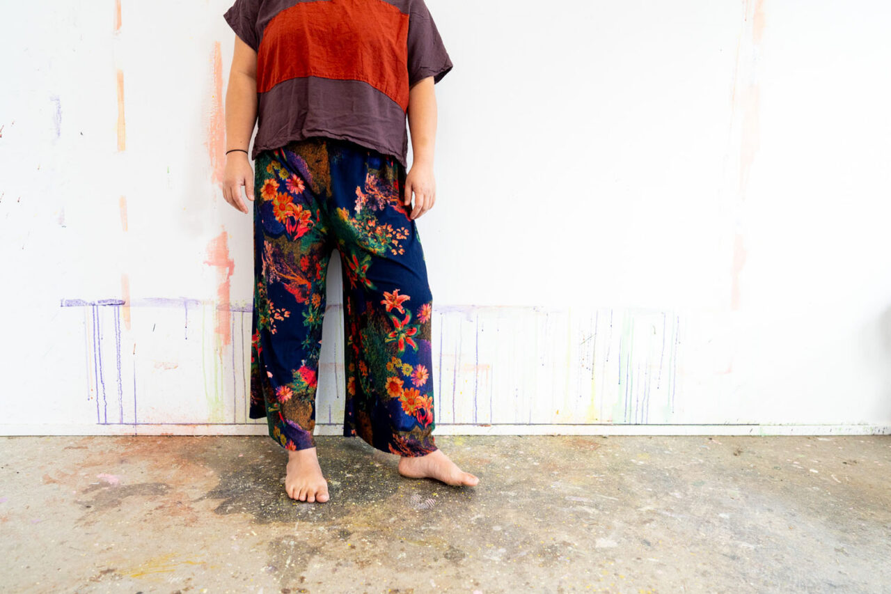 Detail shot of an artist standing barefoot on a paint splattered studio floor wearing floral pants