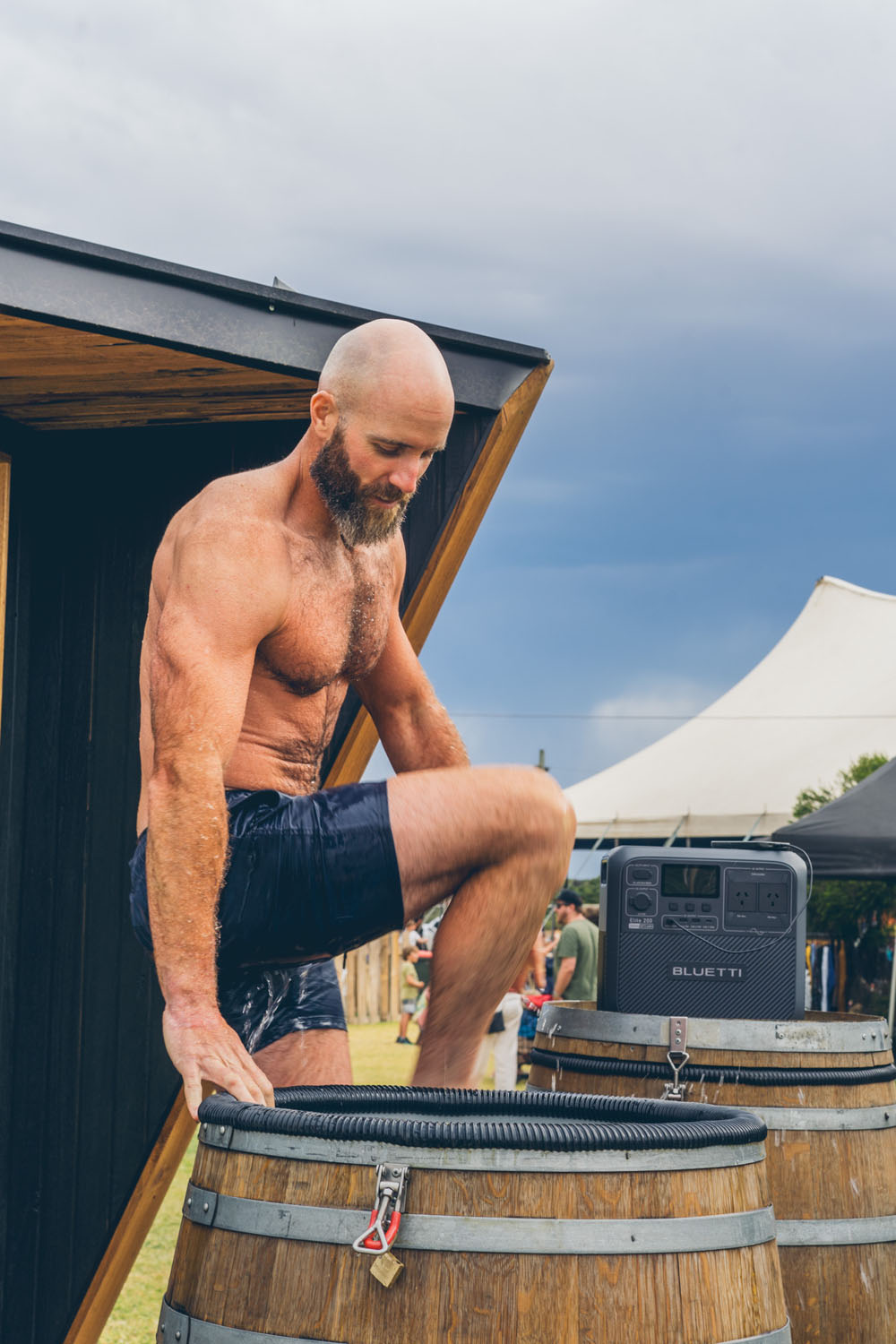 Man climbing into a wooden cold plunge barrel at the NightJar festival