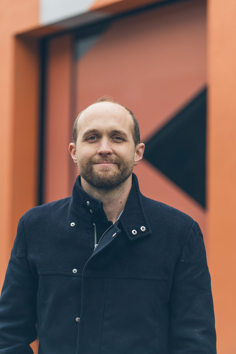 Headshot of a Creaytive team member standing in front of an orange geometric wall
