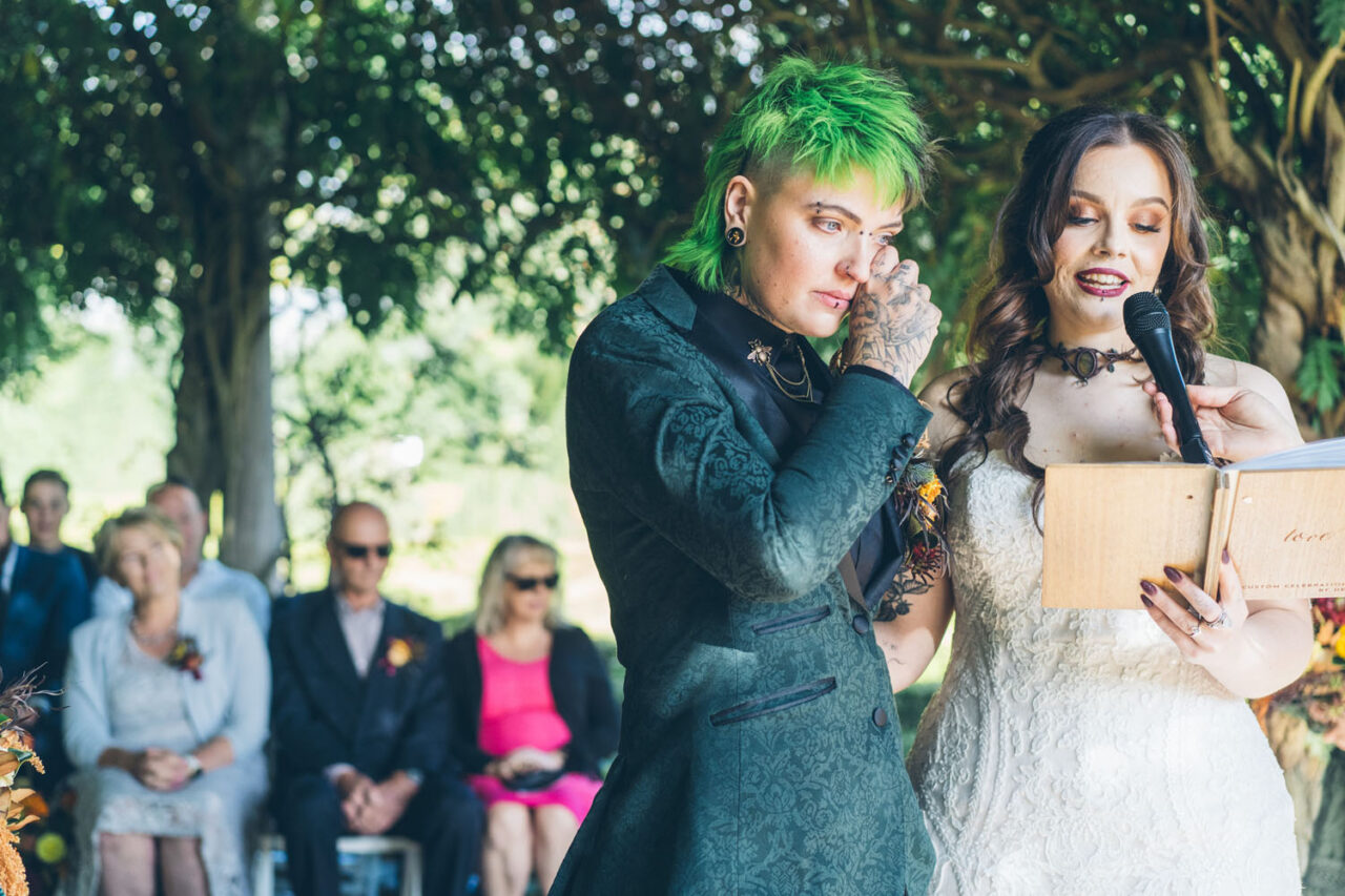 Partner reading vows while their spouse wipes away tears during ceremony.