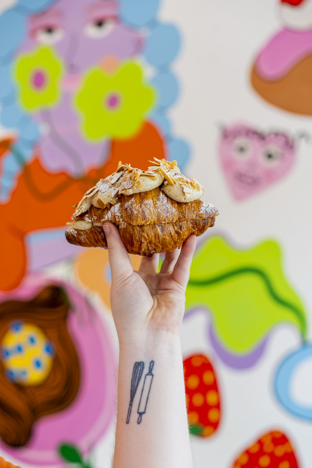 Hand holding an almond croissant in front of colourful mural artwork
