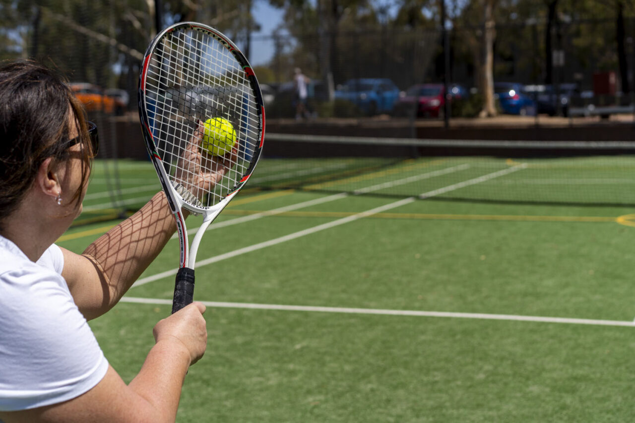 Documentary-style community sport photography capturing a tennis player preparing to serve on an outdoor court