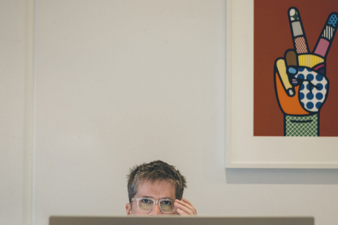 Man working behind a laptop with colourful artwork displayed on the wall