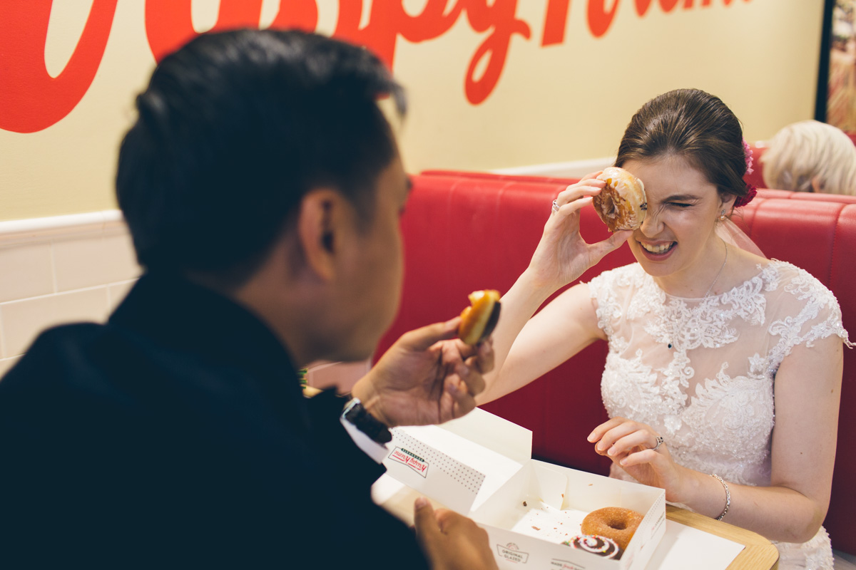 Wedding couple laughing while eating donuts together in a café booth