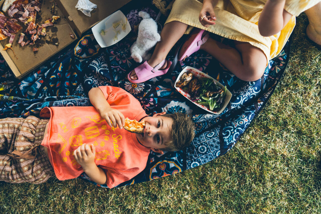 Child eating pizza during a relaxed family picnic, captured as a real, unposed documentary moment