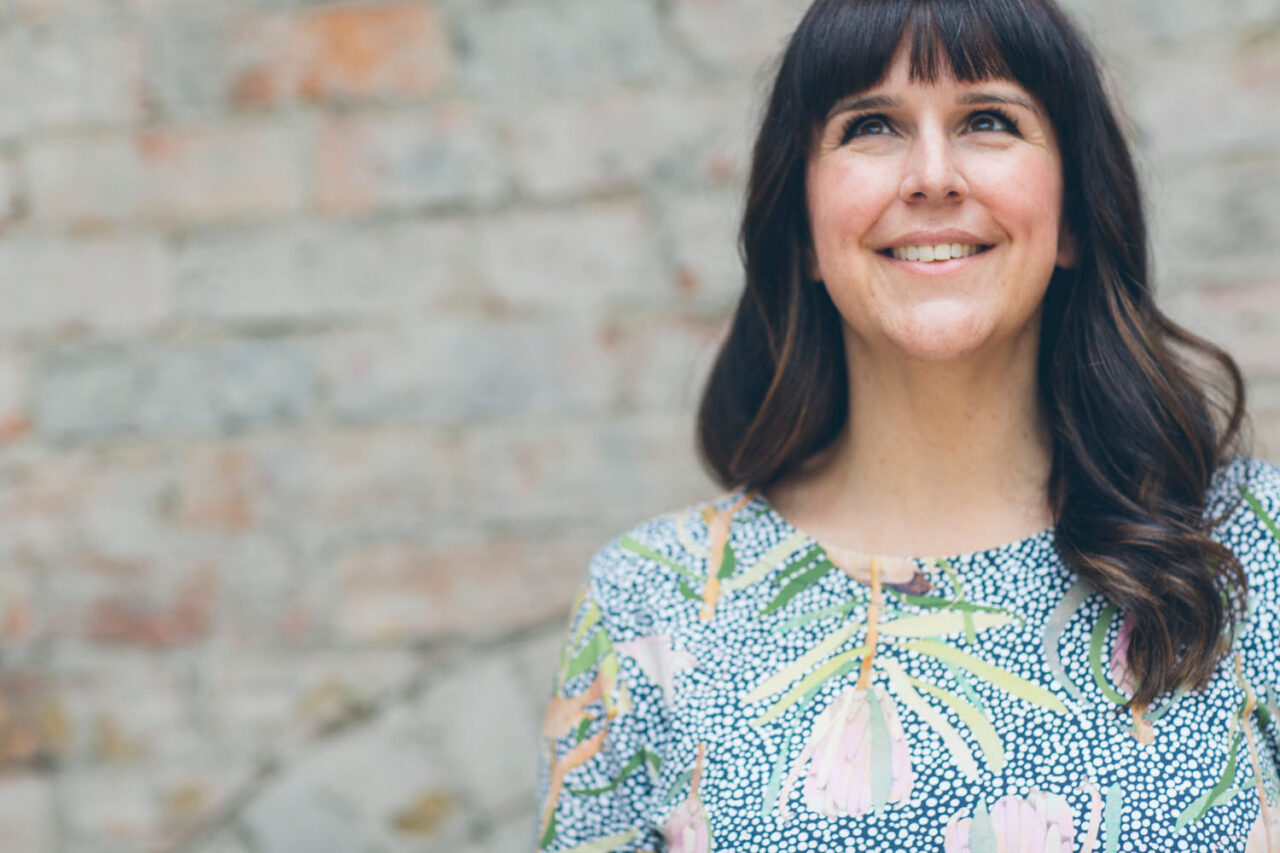 Female entrepreneur smiling in natural light against a textured wall, environmental headshot for personal brand photography.