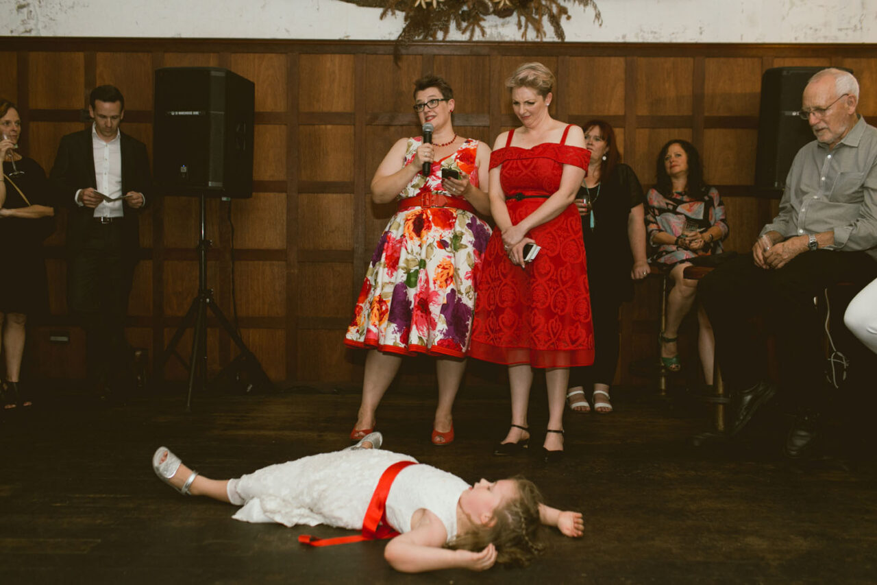 Flower girl lying on the dance floor during wedding speeches, joyful candid wedding moment